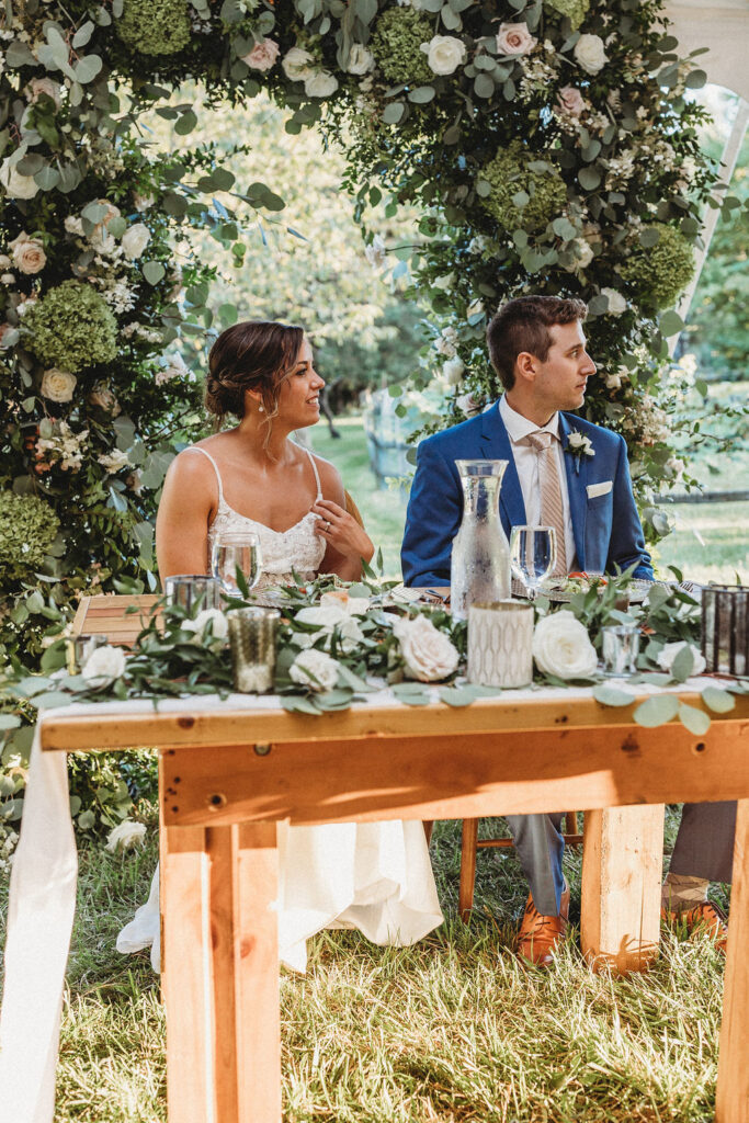 Bride and groom sitting by their reception table decorated with gorgeous floral arrangements