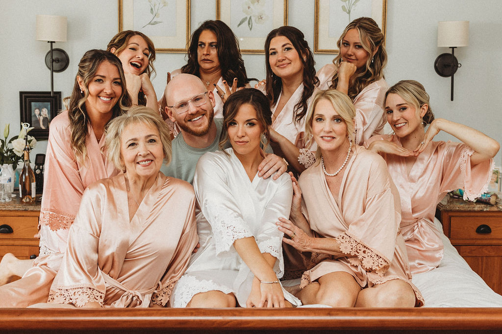 Bride Christine surrounded by her wedding party in the bed, all beaming with joy