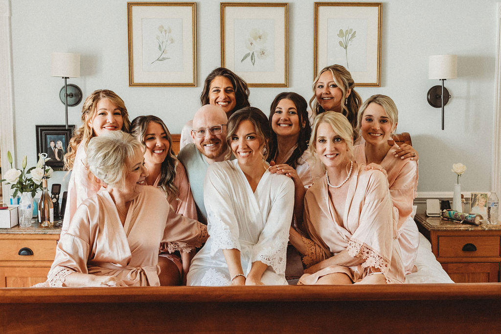 Bride Christine surrounded by her wedding party in the bed, all beaming with joy