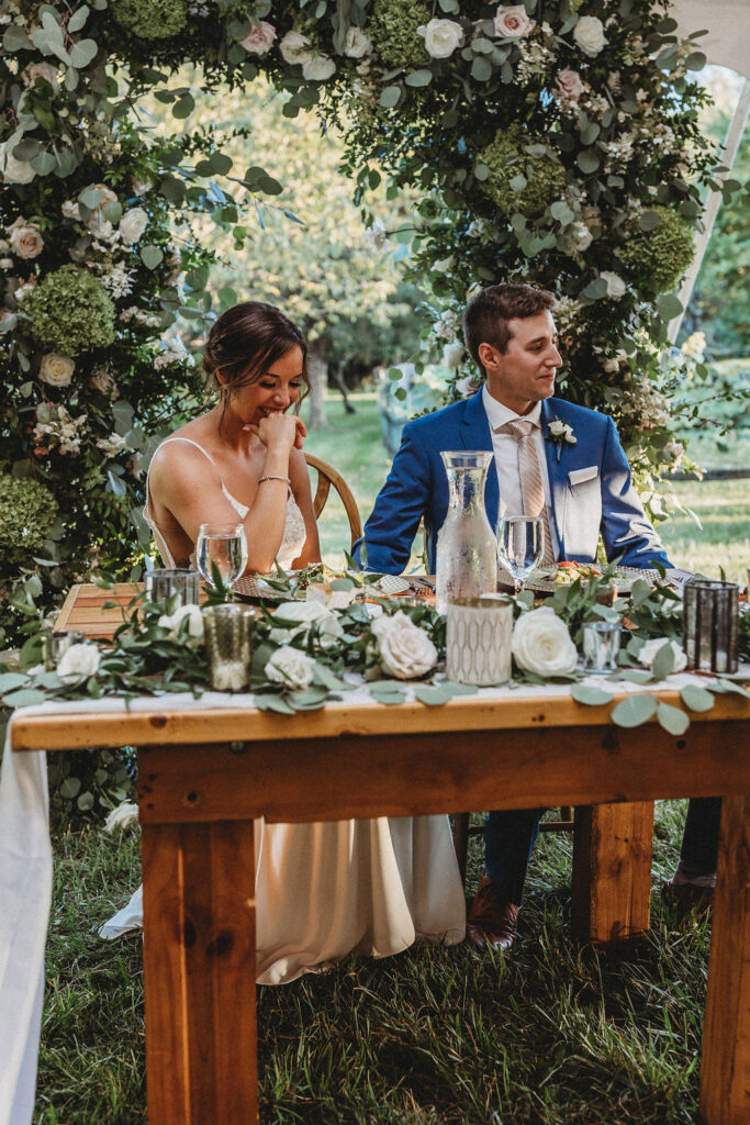 Bride and groom sitting by their reception table decorated with gorgeous floral arrangements