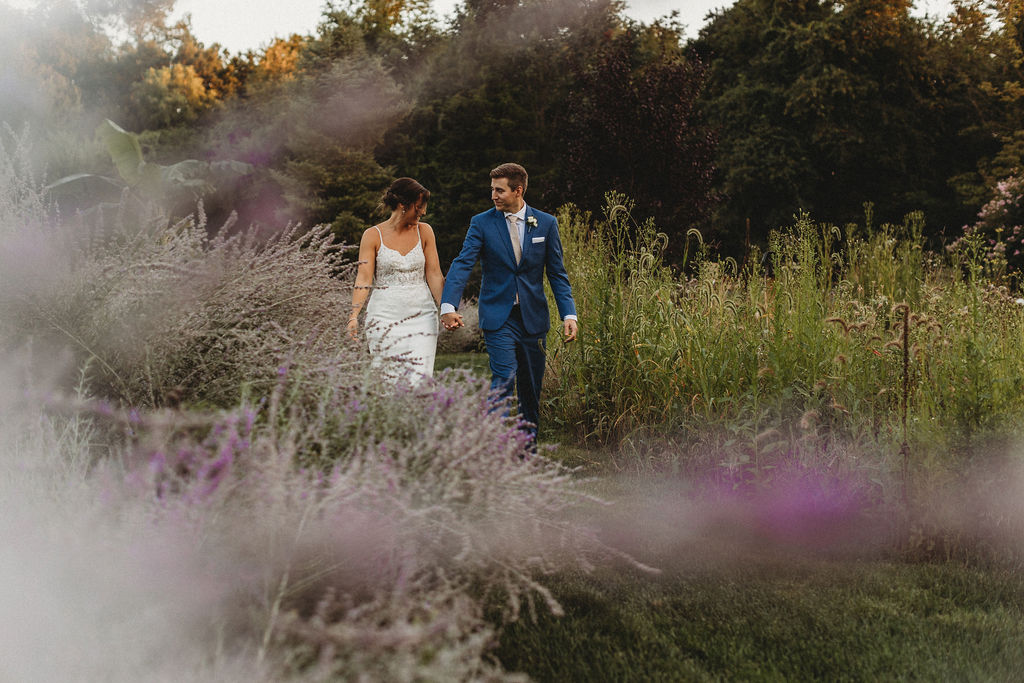 bride and groom holding hands and walking through a field