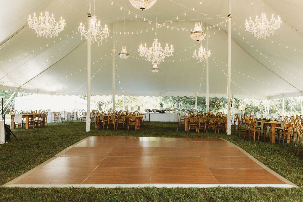 elegant backyard wedding reception set up with a white tent, elegant chandeliers, and rustic table decor